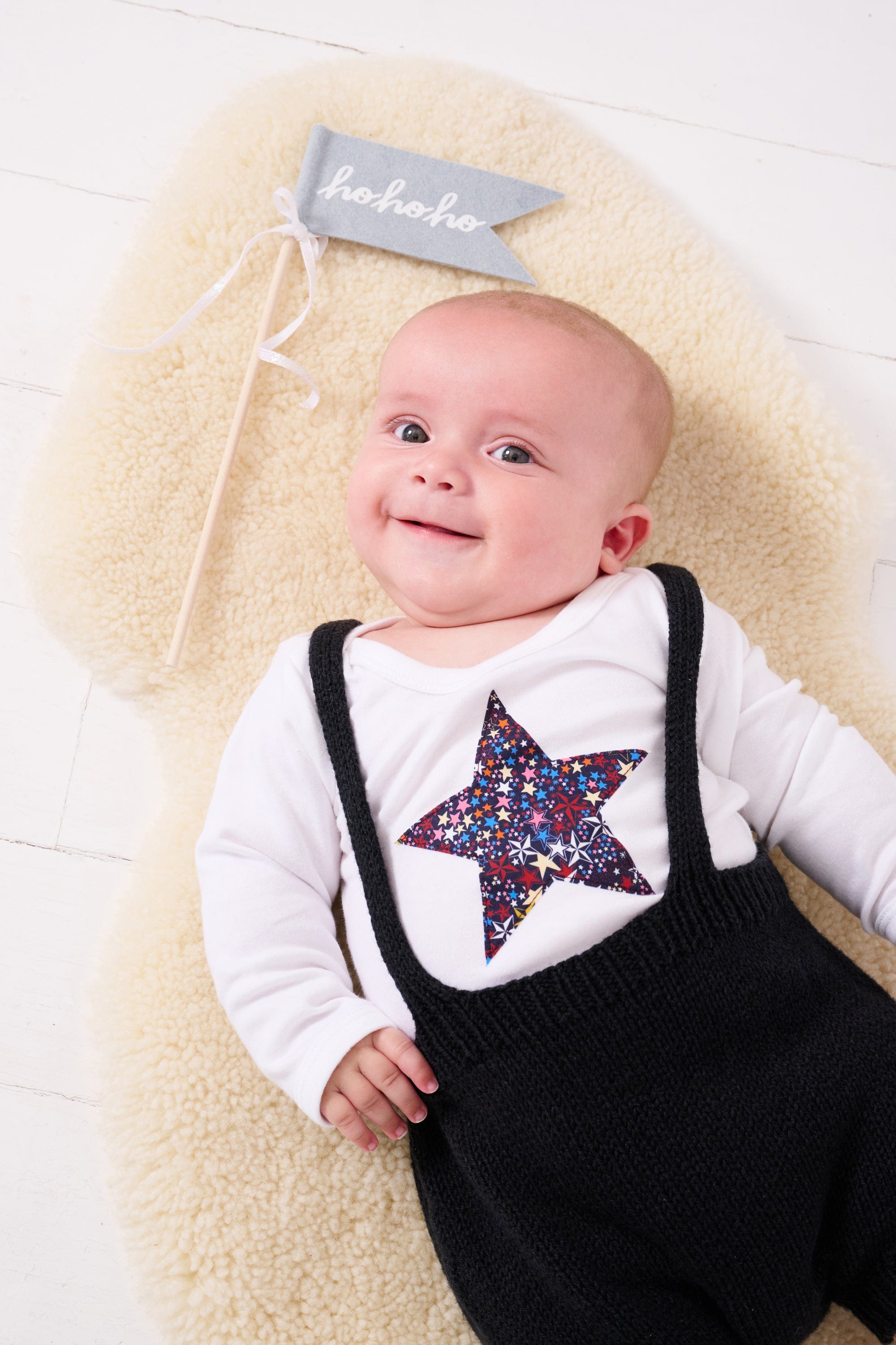 A baby wearing a white bodysuit babygrow with a Liberty Adelajda's Wish print festive star sewn on the front.