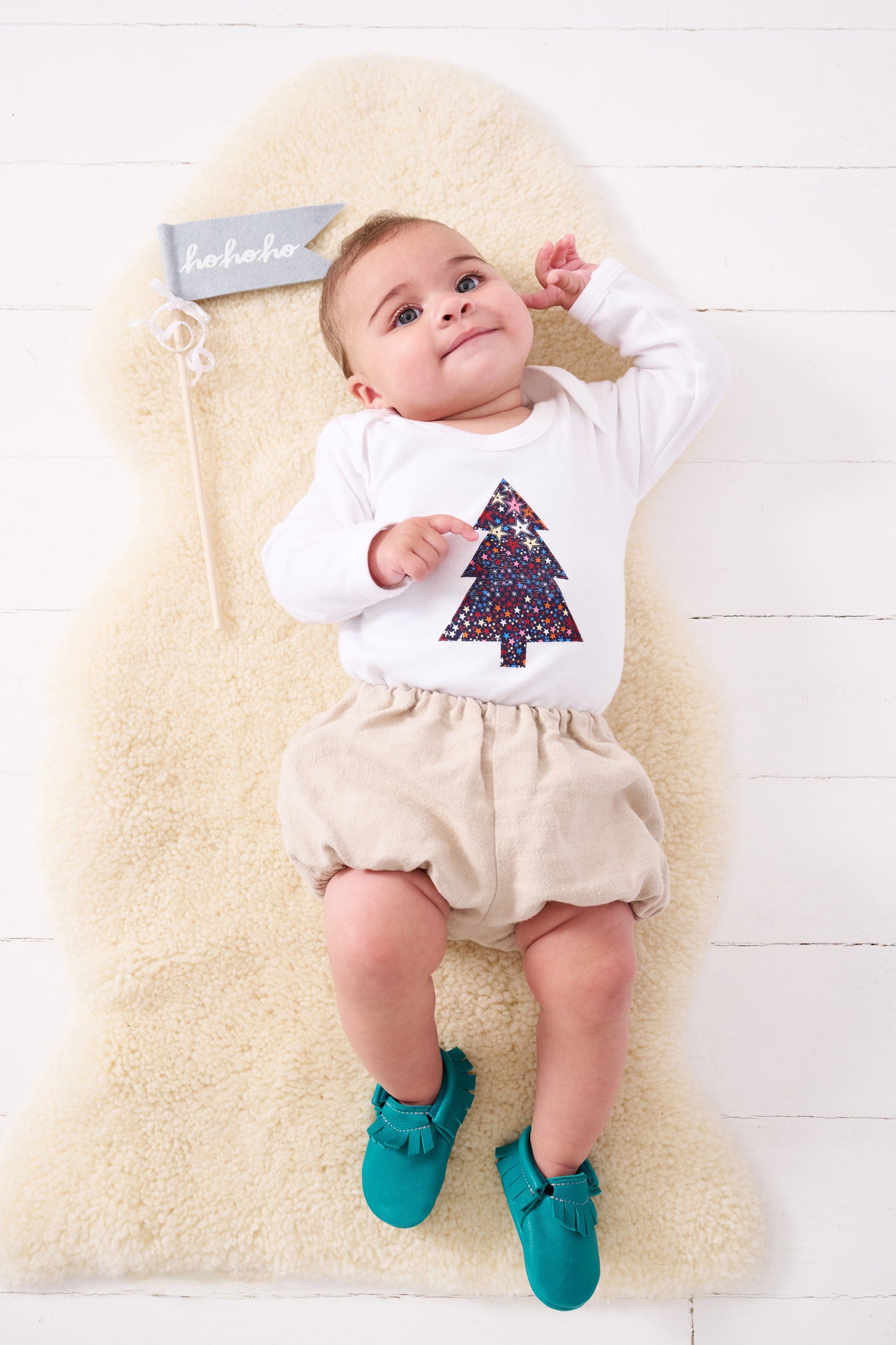 A baby wearing a white bodysuit babygrow with a Liberty Adelajda's Wish print Christmas tree sewn on the front.