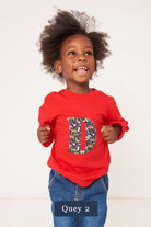 A 3 year old boy wearing a red personalised t-shirt with a liberty animal zoo print letter D appliquéd on the front. 