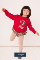 A 2 year old girl wearing a red number t-shirt with a liberty floral number 2 appliquéd on the front. 