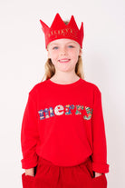 A smiling 5 year old girl wearing a red Christmas t-shirt that says Merry on the front, made from mixed liberty print fabrics.