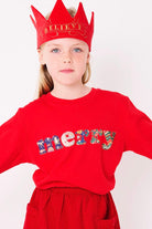 A smiling 5 year old girl wearing a red Christmas t-shirt that says Merry on the front, made from mixed liberty print fabrics.