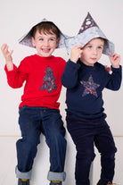 Two children wearing a navy long sleeve christmas t-shirt with a festive star on the front made from Liberty Adelajda's Wish star print on the front and a red one with a Christmas tree on.