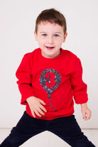 A 3 year old wearing a red cotton t-shirt with a liberty star print birthday balloon on the front with a  number 3 on it.