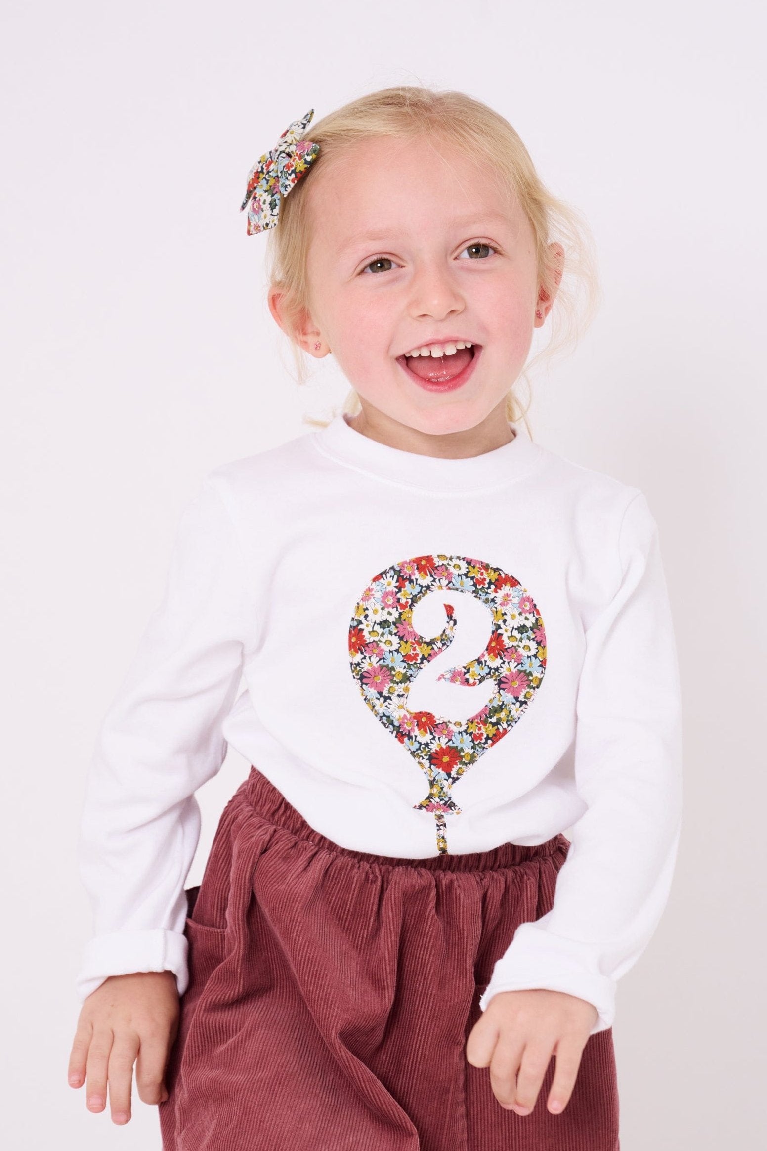 A 2 year old girl wearing a 2nd birthday white t-shirt with a balloon and number 2 on it made from Liberty Floral print fabric.