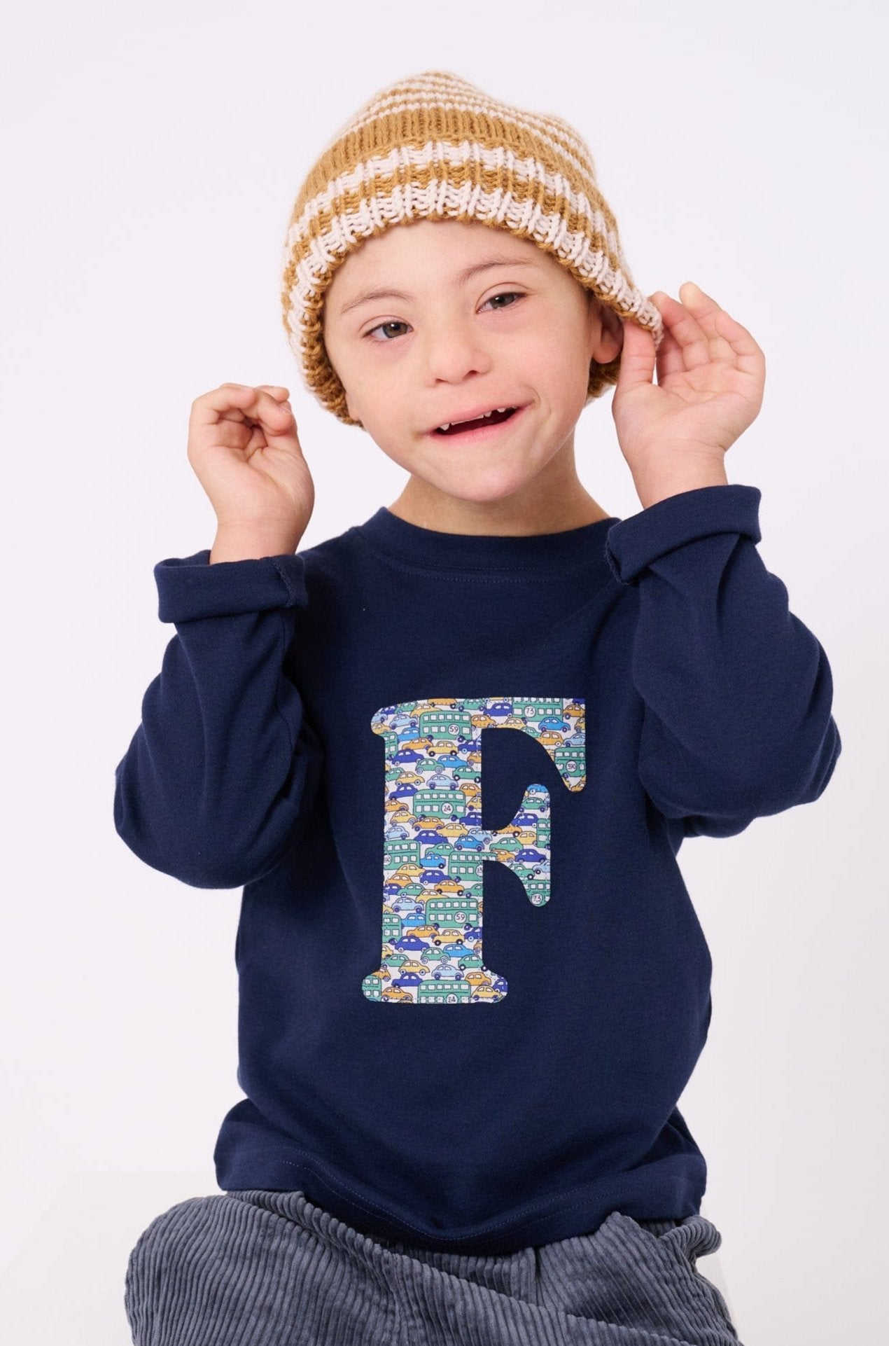 A happy 5 year old child wearing a personalised cotton long sleeve navy t-shirt  with his initial on the front made from Liberty cars print.