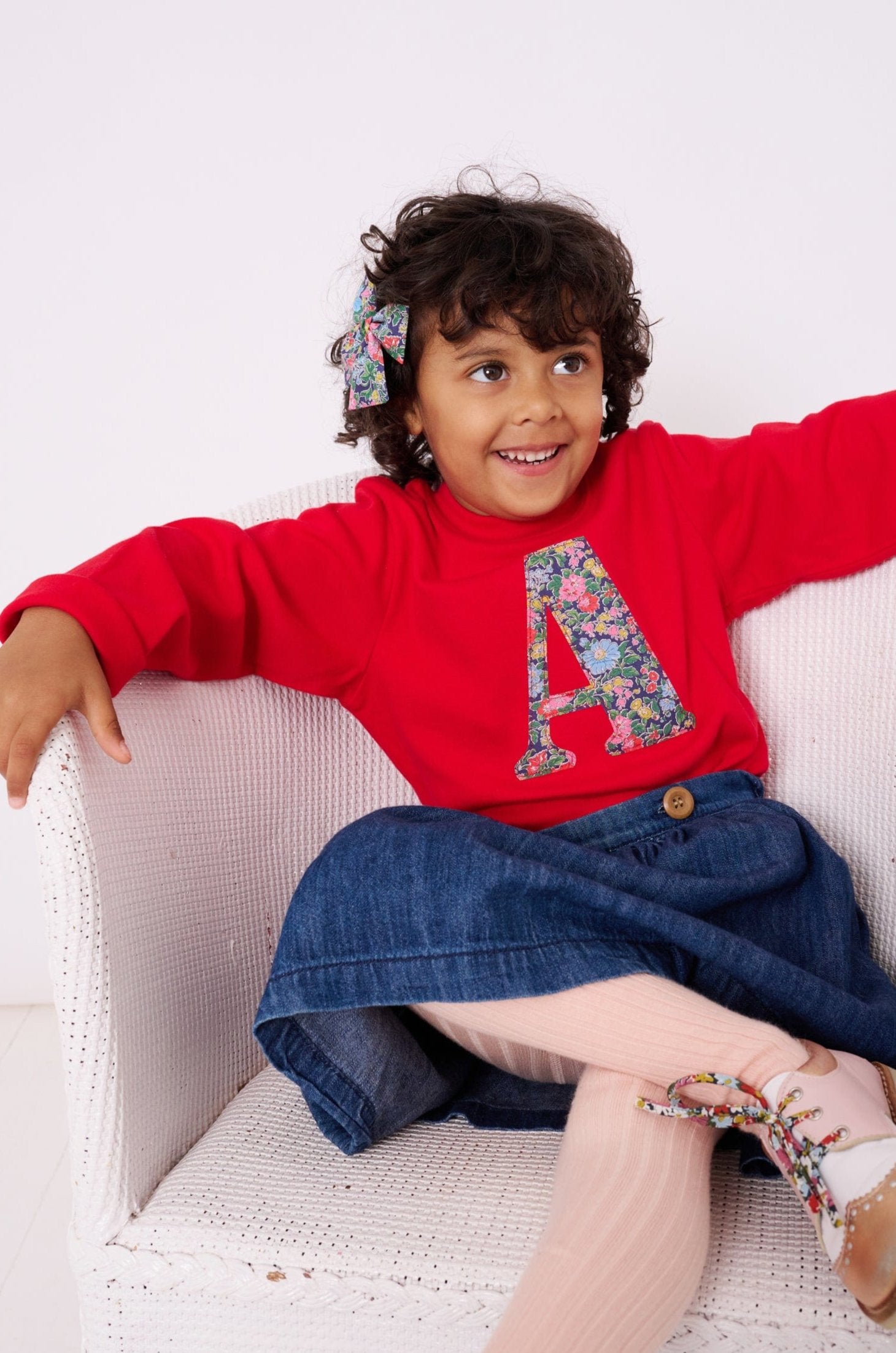 A 4 year old girl wearing a personalised red t-shirt with her initial on in a Liberty floral fabric.