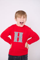 A 5 year old boy wearing a personalised red t-shirt with an initial made from a liberty vintage cars print on the front.