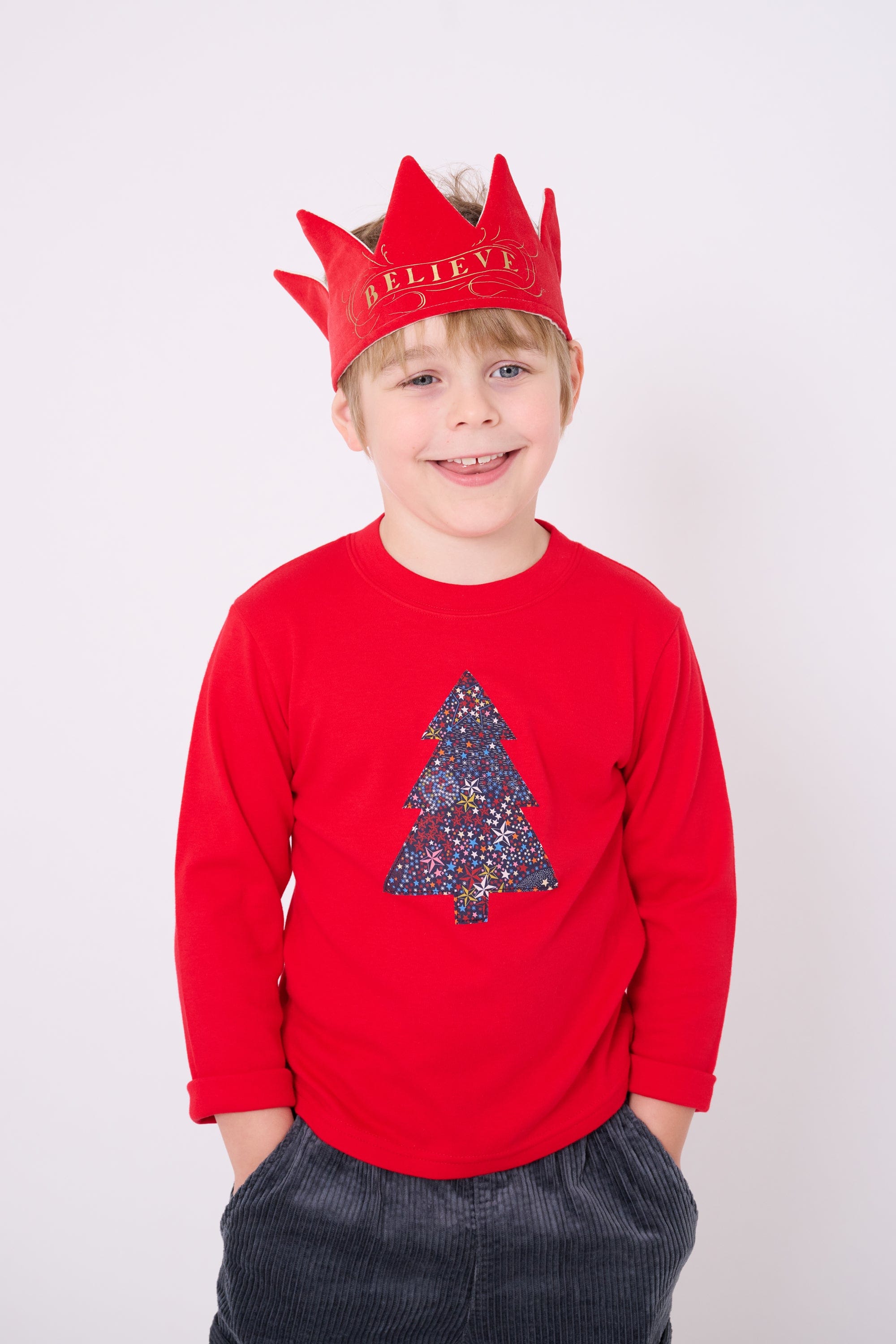 A 4 year old boy wearing a festive red cotton t-shirt with a christmas tree made from Liberty star Adelajda's Wish fabric appliquéd on the front.