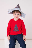 A 4 year old boy wearing a festive red cotton t-shirt with a christmas tree made from Liberty star Adelajda's Wish fabric appliquéd on the front.