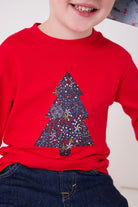 A 4 year old boy wearing a festive red cotton t-shirt with a christmas tree made from Liberty star Adelajda's Wish fabric appliquéd on the front.