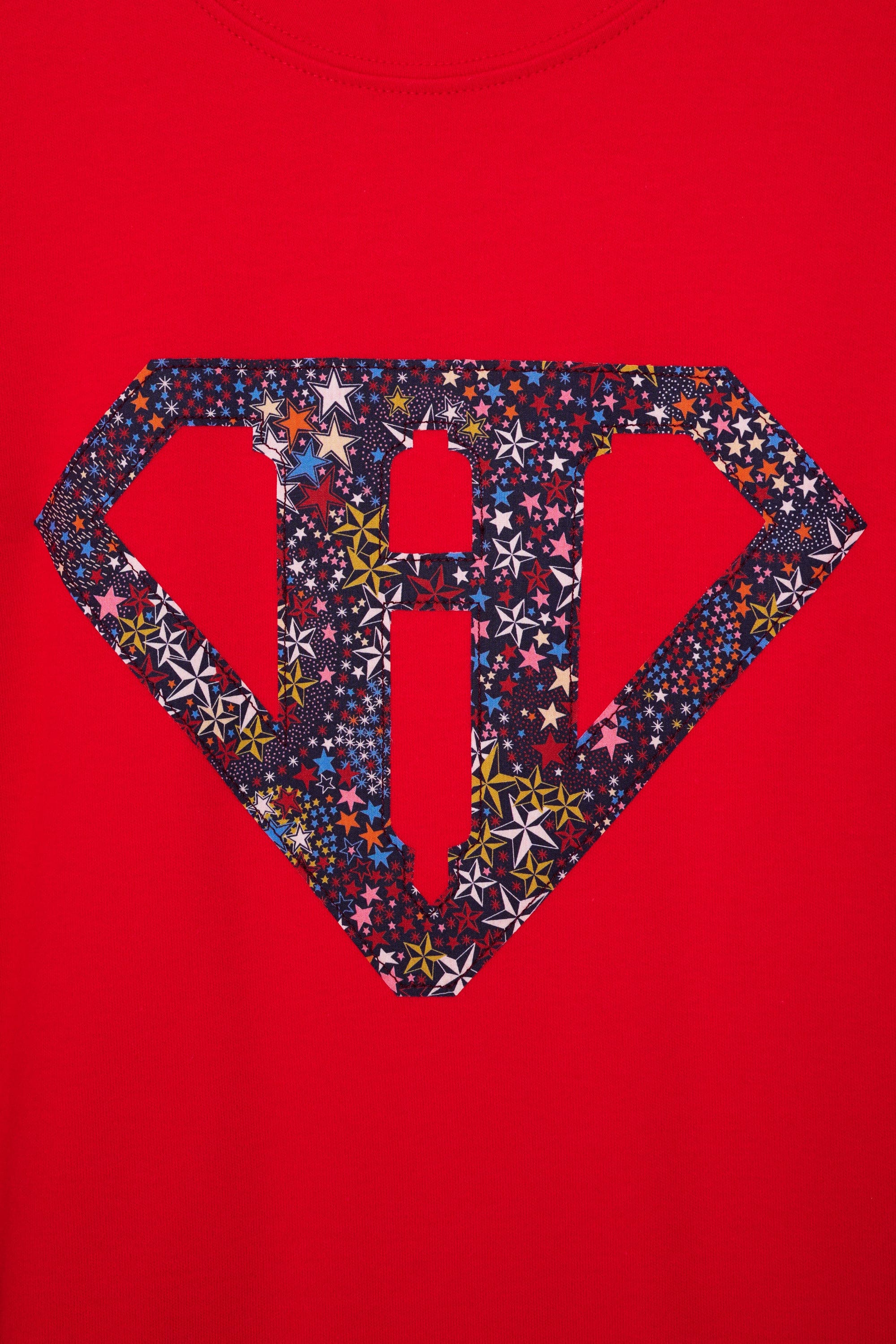 A close up of a red cotton personalised t-shirt with his initial in a superhero emblem Liberty star Adelajda's Wish fabric appliquéd on the front.