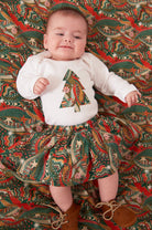 A baby wearing a white bodysuit babygrow with a Liberty My Little Star print festive Christmas tree sewn on the front.