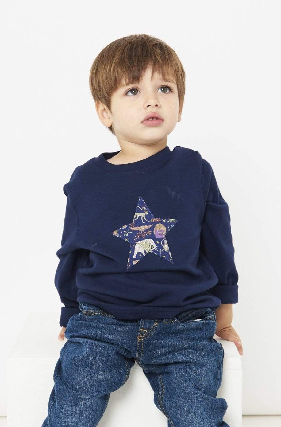 A 3 year old boy wearing a navy long sleeve christmas t-shirt with a festive star on the front made from Liberty Christmas print on the front.