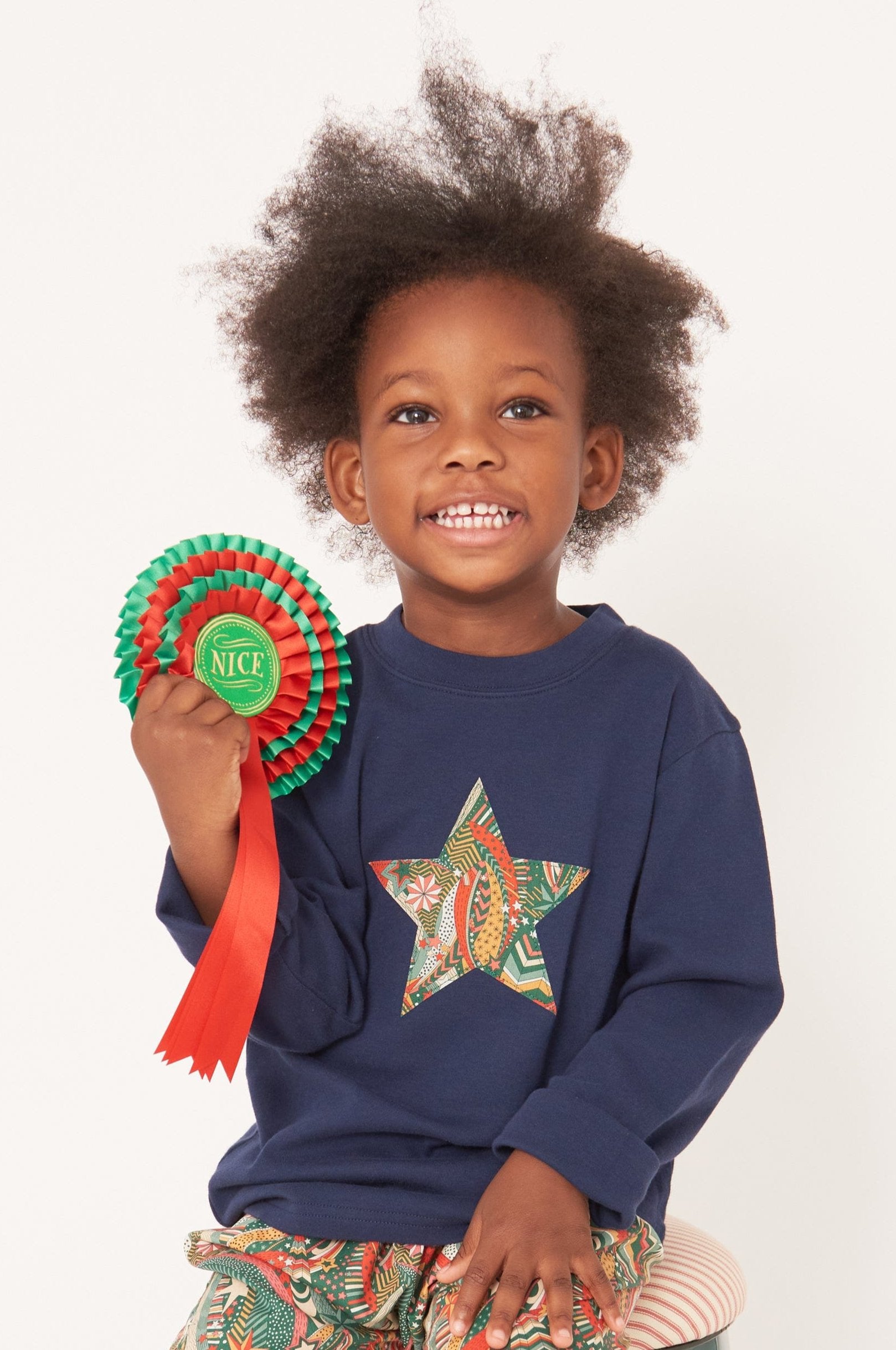 A 3 year old boy wearing a navy long sleeve christmas t-shirt with a festive star on the front made from Liberty My Little Star print on the front.
