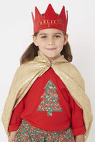 A smiling 5 year old girl wearing a festive red t-shirt with a Christmas tree on the front made from Liberty Glitter Wiltshire berry fabric.