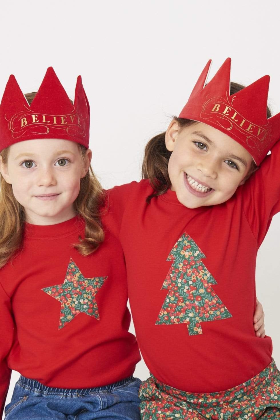 2 smiling 5 year old girls wearing festive red t-shirts with a star and Christmas tree on the front made from Liberty Glitter Wiltshire berry fabric.