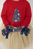 A girl holding a liberty cracker wearing a festive red t-shirt with a christmas tree on the front made from Liberty Christmas fabric.